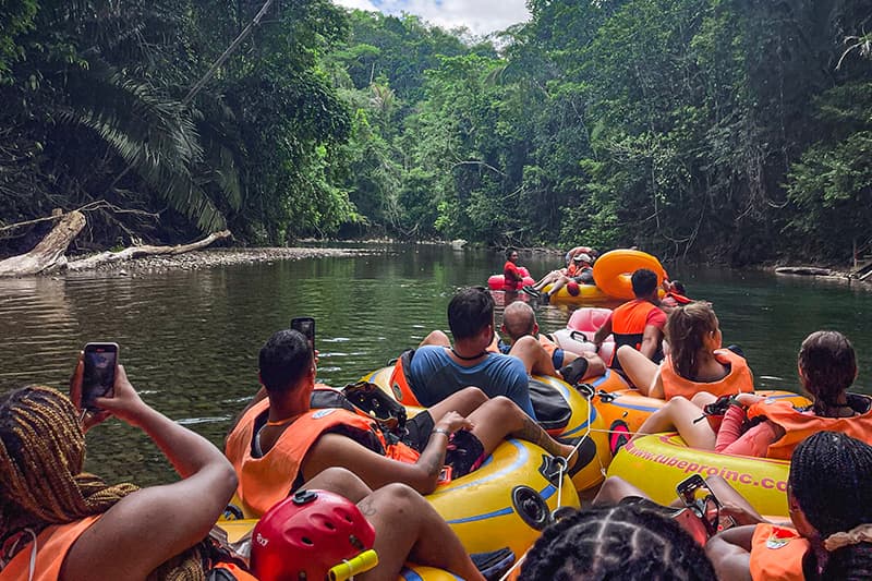 A group of people in colorful life jackets float down a serene river surrounded by lush greenery. A group of people in colorful life jackets float down a serene river surrounded by lush greenery.