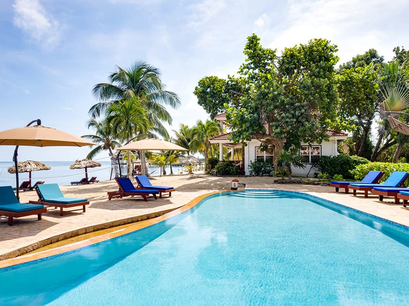 A tranquil beachfront villa with a crystal-clear pool surrounded by palm trees and sun loungers.