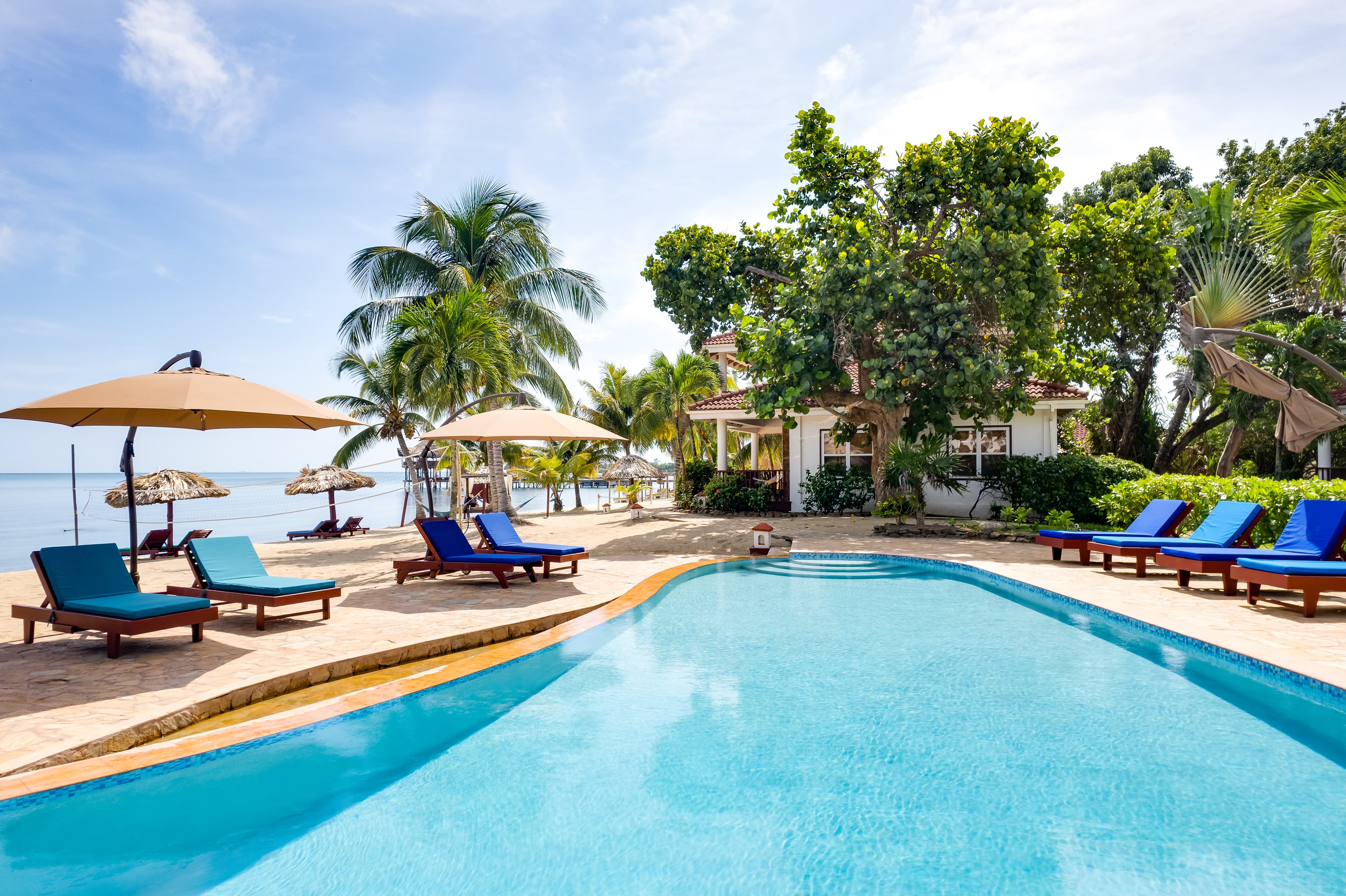 Pool image with pool chairs, lodging and ocean in background, with buildings.