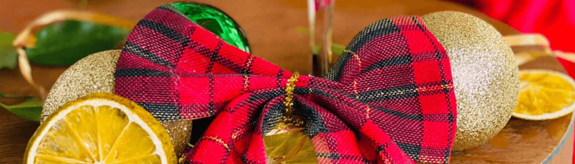 A festive arrangement featuring gold ornaments, a red plaid bow, and dried orange slices.