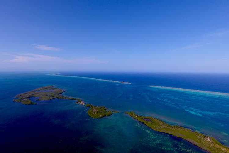 Aerial view of a vibrant blue sea with scattered green islands and a clear sky.