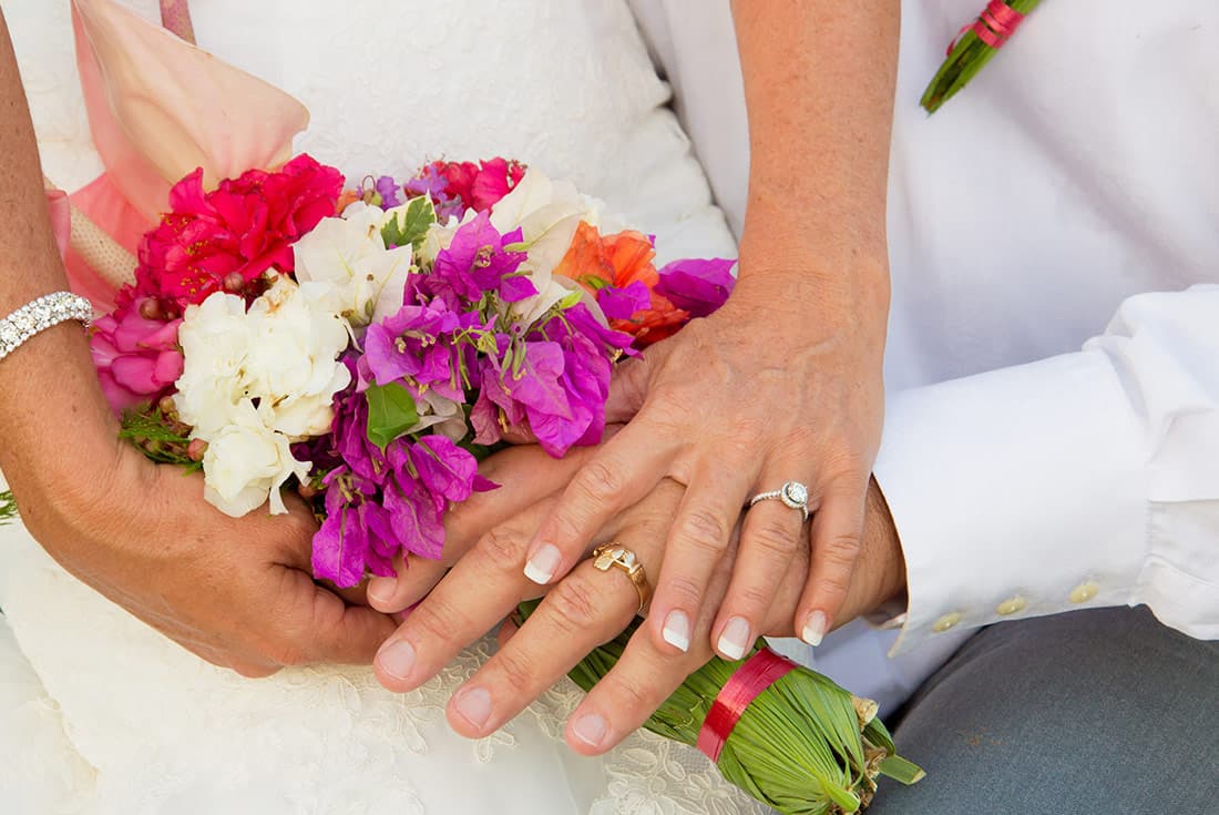 Newlyweds' hands holding a vibrant wedding bouquet