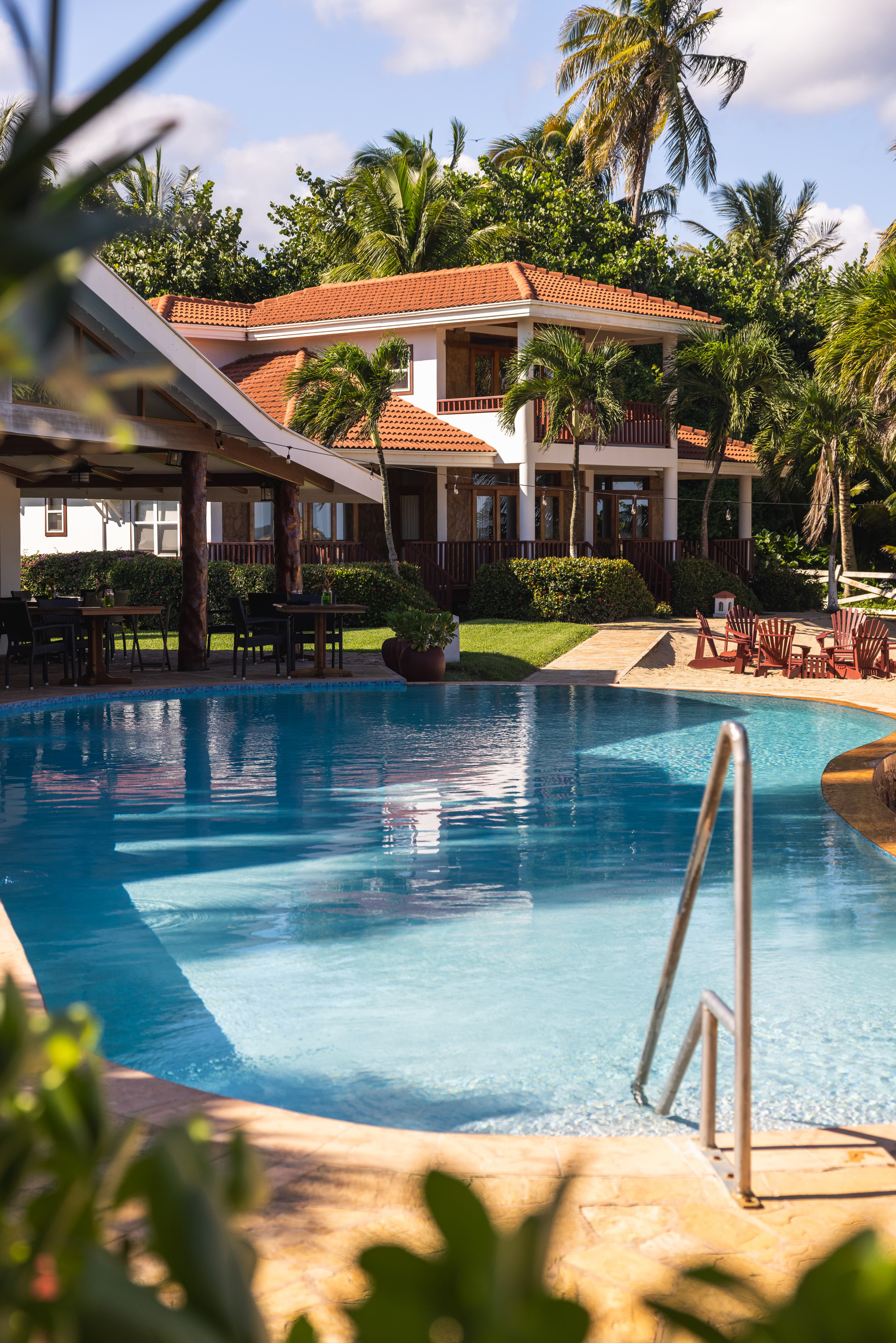 A pool surrounded by palm trees and a red-roofed building.