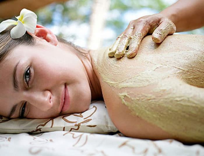 A pretty brunette woman with a white flower in her hair receives a spa body wrap service.