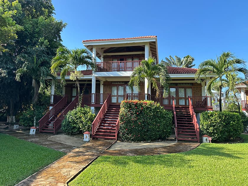 A tropical house with a red staircase surrounded by lush greenery under a clear blue sky.