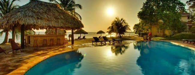 Tropical resort pool at sunset with palm trees and thatched-roof cabana. Tropical resort pool at sunset with palm trees and thatched-roof cabana.