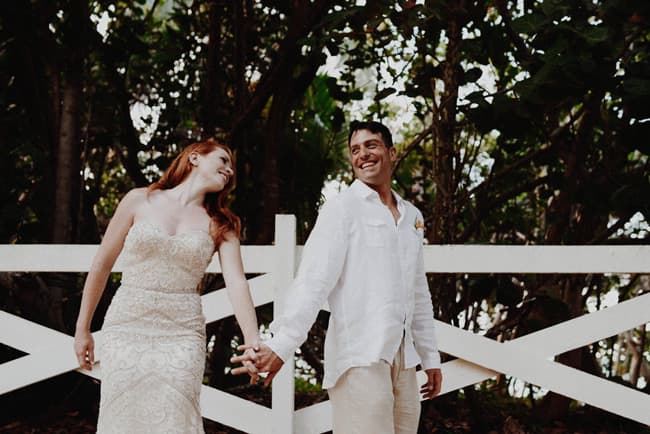 A bride and groom hold hands and smile at each other in a lush, outdoor setting.