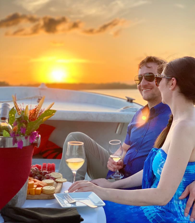 A couple enjoys drinks and a sunset while seated on a boat.