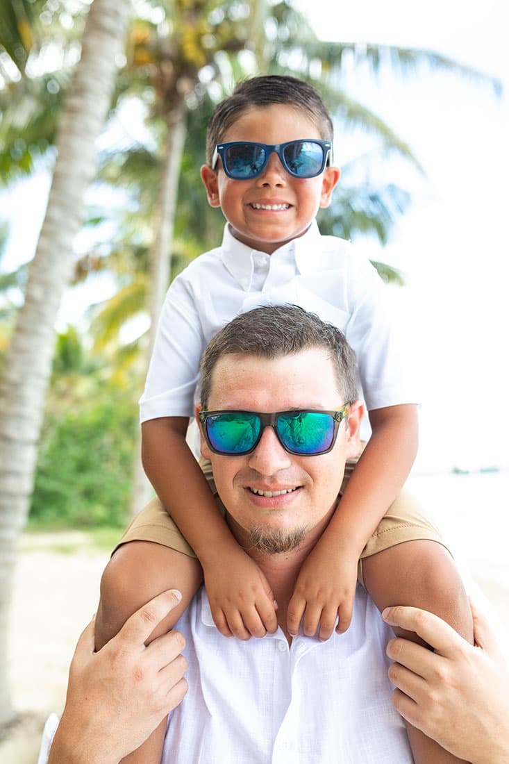 A dad holds a young boy on his shoulders. Both are wearing black sunglasses and white button down shirts.