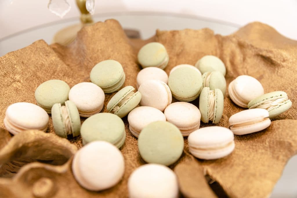 An assortment of cream and pale green macarons rests artfully in a brown-paper lined dish.