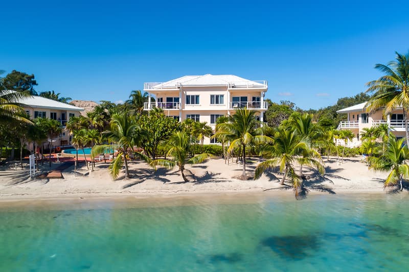 Aerial view of a beachfront property surrounded by palm trees and calm turquoise water.