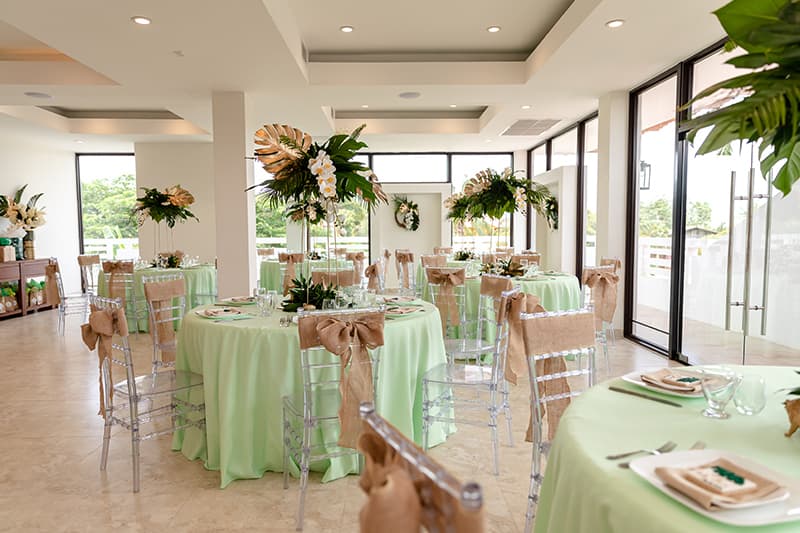 A beautifully set dining area featuring mint green tablecloths, elegant floral centerpieces, and large windows for natural light.
