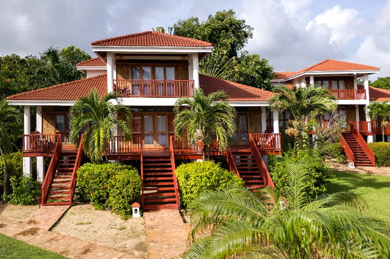 A tropical two-story villa surrounded by lush greenery and palm trees.