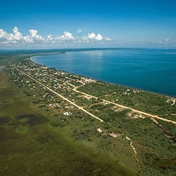 An aerial view of a coastal town with a large body of water in the background. The town is surrounded by lush green vegetation, and there are roads leading to the water.