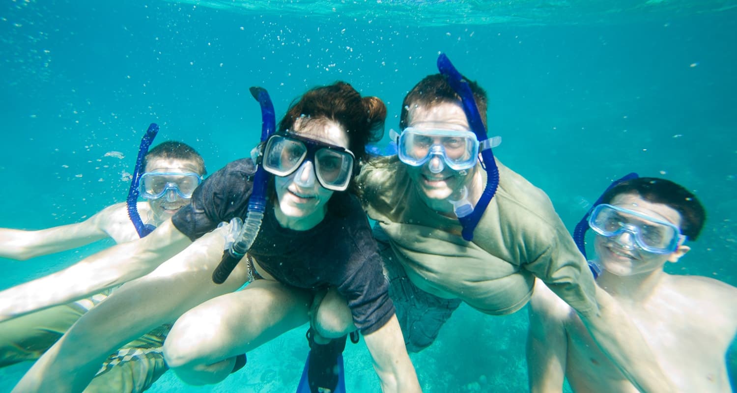 4 men and boys with blue snorkels in water posing for the camera.