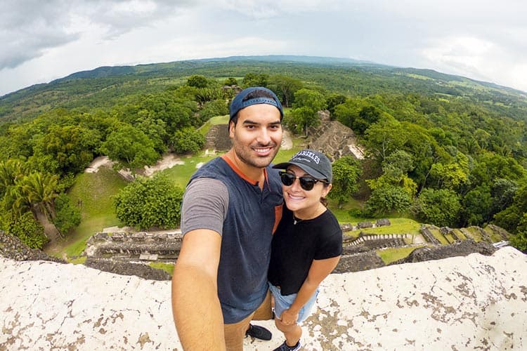A couple poses for a selfie with a lush, green landscape in the background.