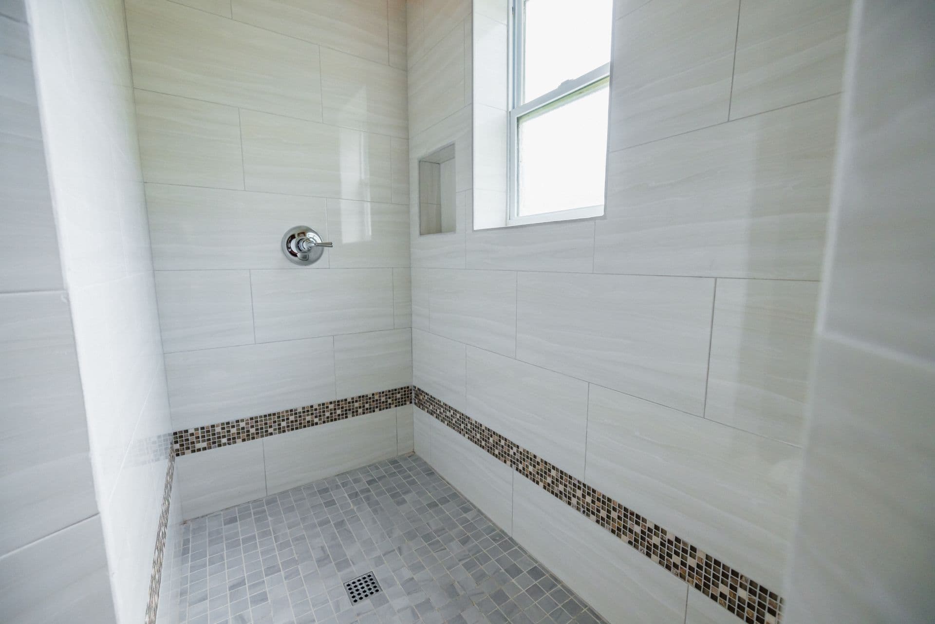A modern shower with white tiled walls and a mosaic border.