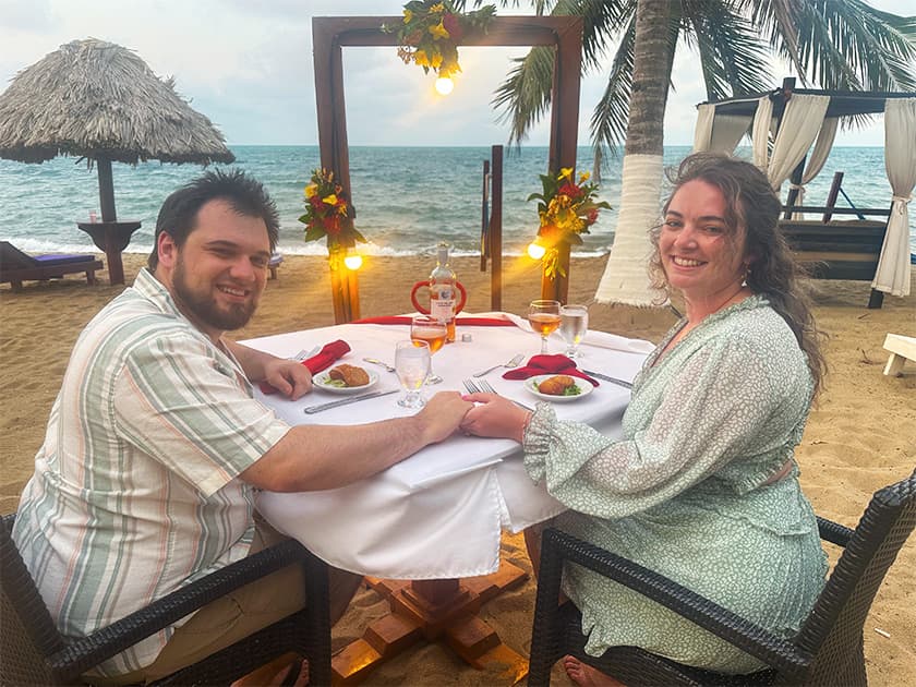 A couple smiles at each other while seated at a romantic beachside dinner table.