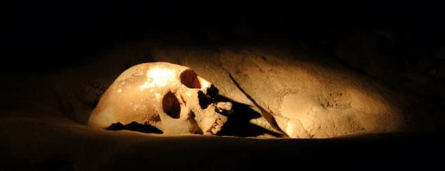 A human skull illuminated by soft light, partially buried in sand. A human skull illuminated by soft light, partially buried in sand.