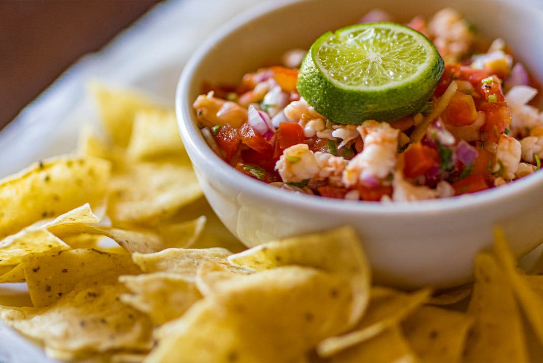 The image shows a bowl of ceviche, a popular Latin American dish made with raw fish marinated in citrus juices. This particular ceviche seems to be made with shrimp, as it contains small pieces of cooked shrimp.