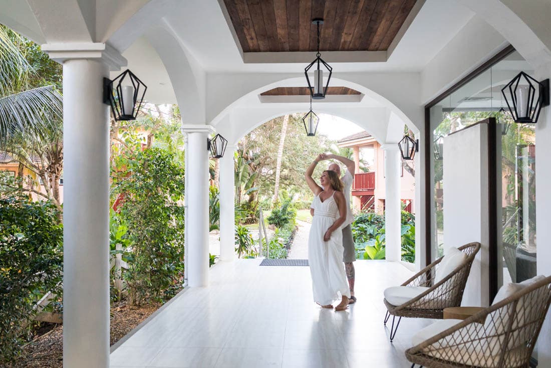 A mature couple embrace inside a beautiful colonnade with a wooden ceiling, and wrought-iron light fixtures.