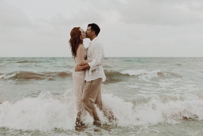A couple in beachwear kisses while standing in the ocean waves.