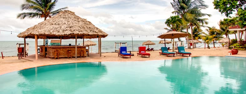A tranquil beach scene featuring a pool, thatched-roof bar, and colorful lounge chairs under palm trees. A tranquil beach scene featuring a pool, thatched-roof bar, and colorful lounge chairs under palm trees.