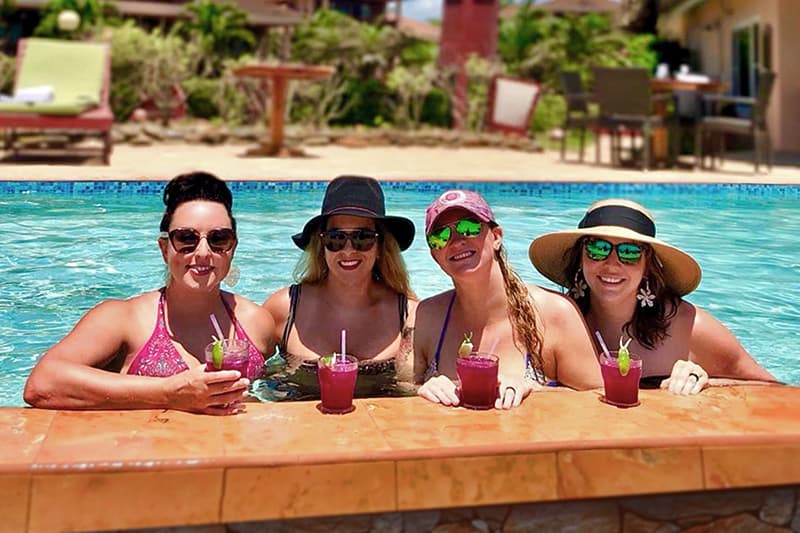 Four women enjoy drinks while relaxing in a pool on a sunny day. Four women enjoy drinks while relaxing in a pool on a sunny day.