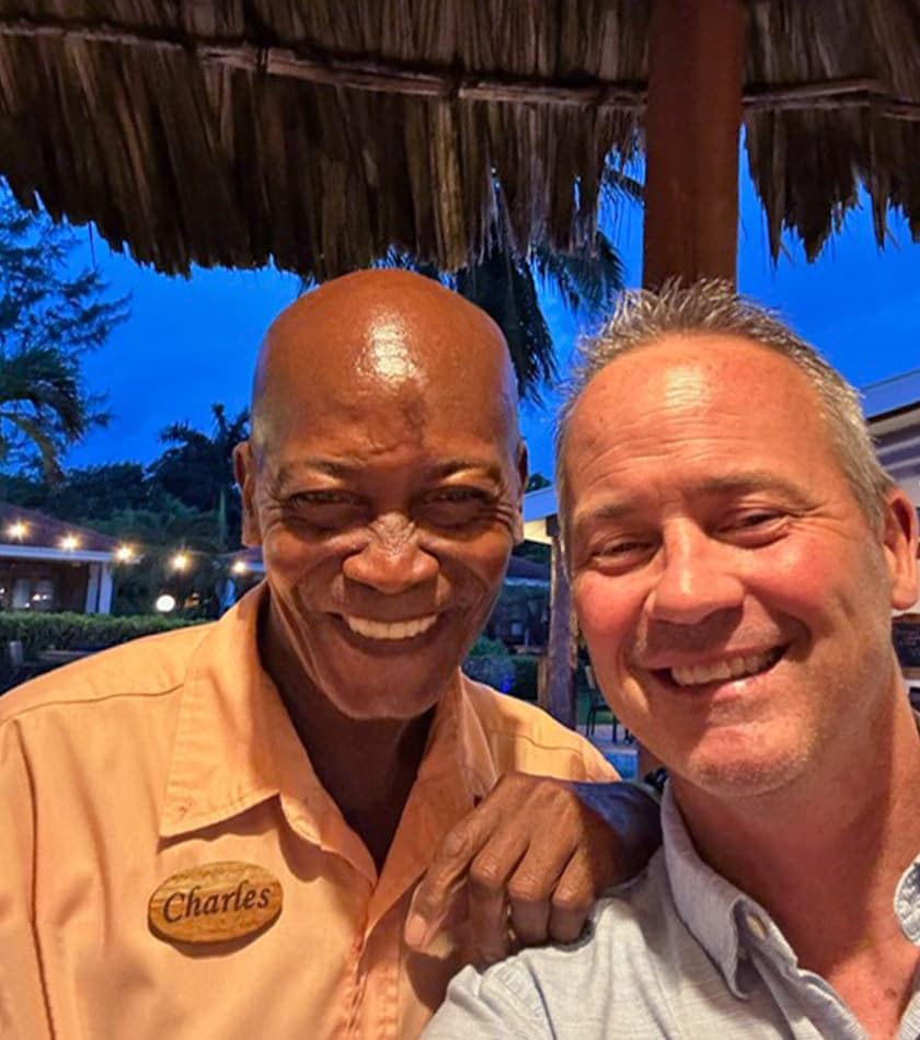 Guest takes selfie with friendly Belizean Dreams bartender Charles under thatched roof.